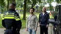 Politieagent kijkt naar twee mannen. Kale man draagt blauw sportjack.