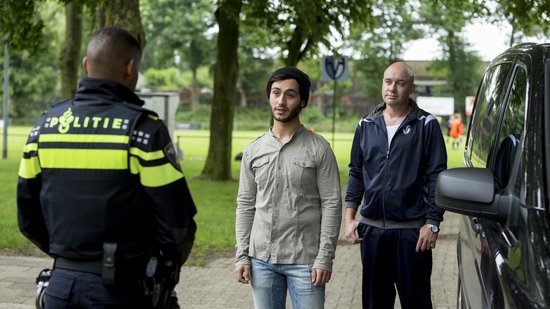 Politieagent kijkt naar twee mannen. Kale man draagt blauw sportjack.