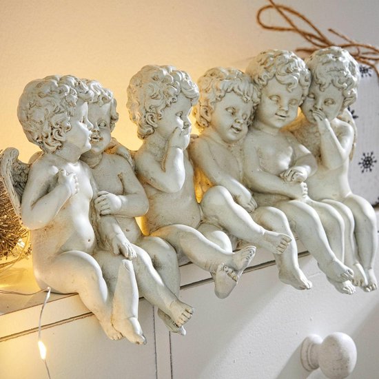 Zes witte cherubijnbeeldjes zitten op een witte commode met kerstverlichting.