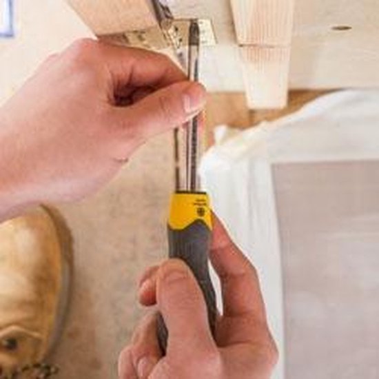 Handen gebruiken een Stanley Cushion Grip schroevendraaier met geel handvat om een scharnier vast te zetten.