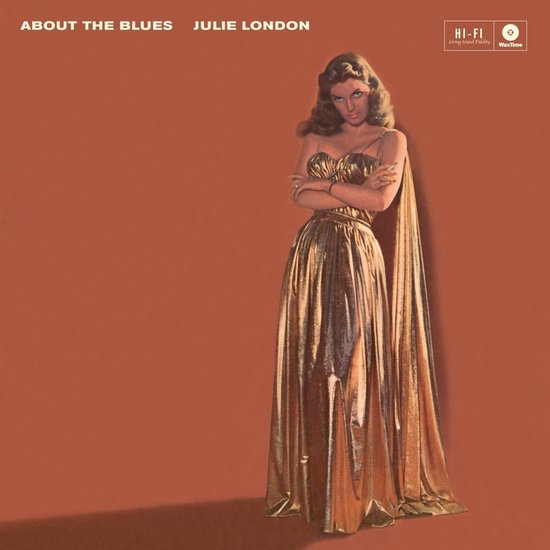 Julie London in een glanzende gouden jurk met strapless top, armen gekruist, voor een oranje achtergrond.