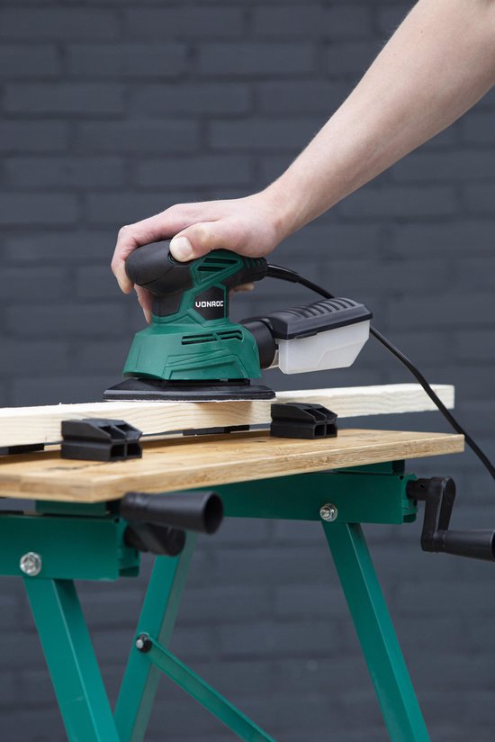 Hand met groene VONROC multislijper die een houten plank schuurt op een werkbank.
