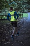 Man joggend in het park met een fluoriserend geel reflectiehesje over een blauw shirt.