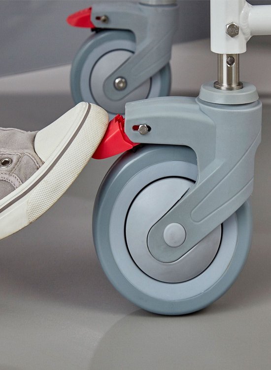 Voet van een grijze sneaker die een rode rem op een rolstoelwiel indrukt.
