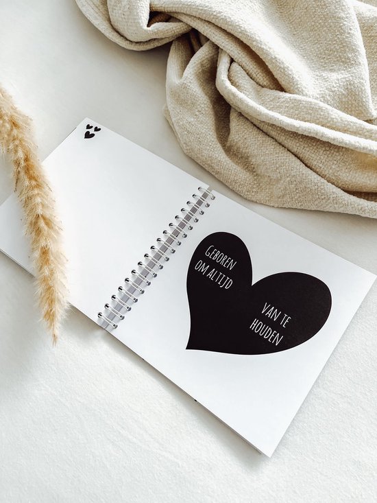 Open boek met een zwart hart. Tekst: 'Geboren om altijd van te houden'. Twee kleine hartjes linksboven.