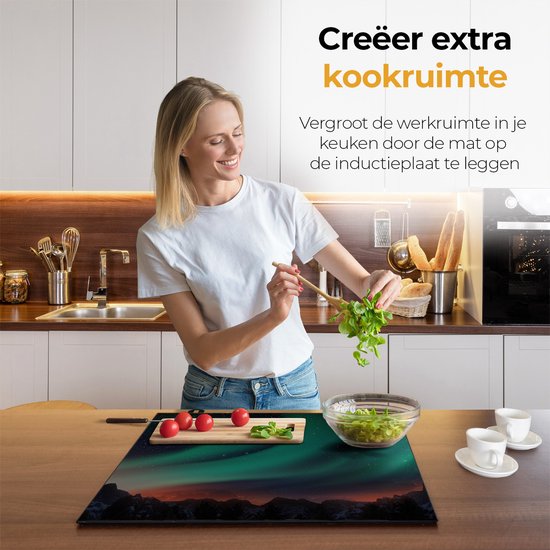 Een vrouw plaatst een beschermmat met Noorderlicht-afbeelding op een inductiekookplaat in een keuken.