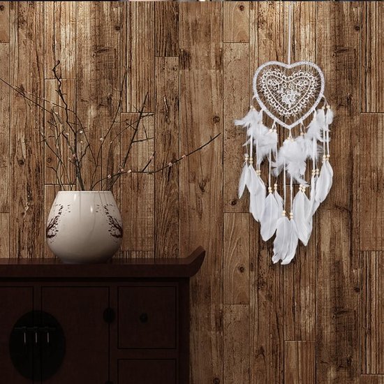 Attrape-rêves blanc en forme de cœur avec dentelle, perles et plumes blanches, suspendu à un mur en bois.