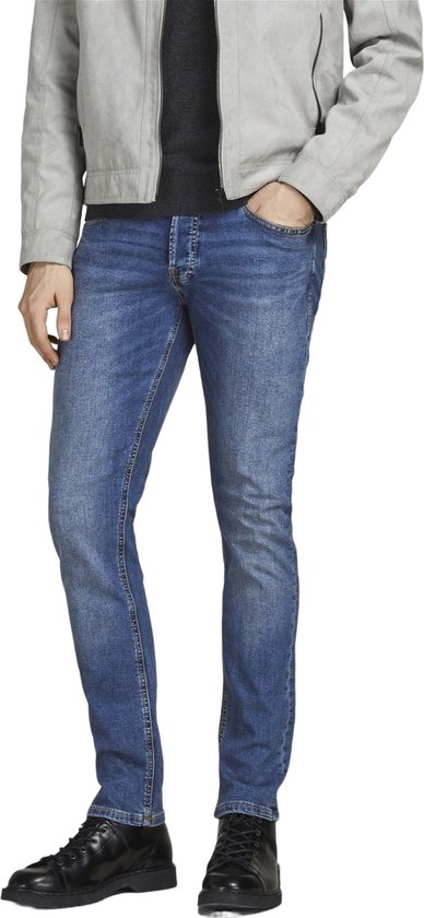 Man met de hand in de zak van een blauwe jeans, met grijze jas.