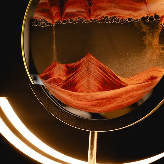 Close-up van rode en oranje zandkunst in een rond glas, met een halvemaanvormige lamp.