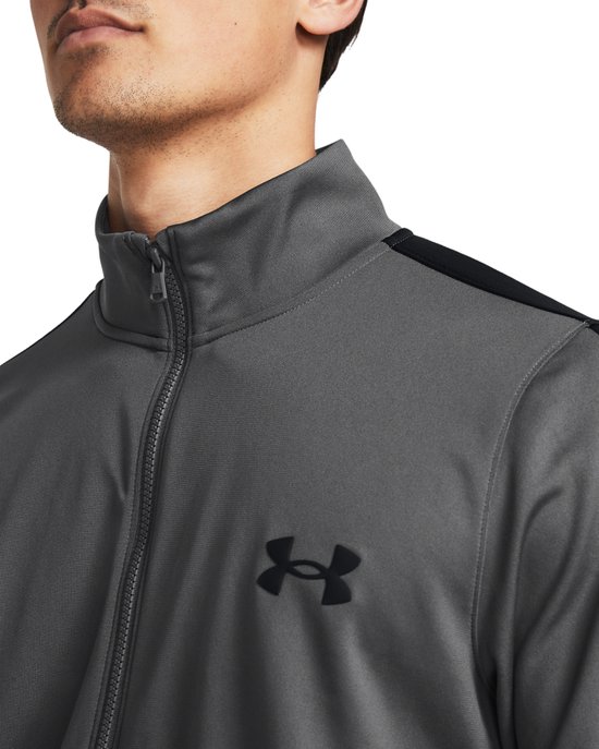 Grijs trainingsjack met zwarte strepen op de mouwen en een zwart Under Armour logo.