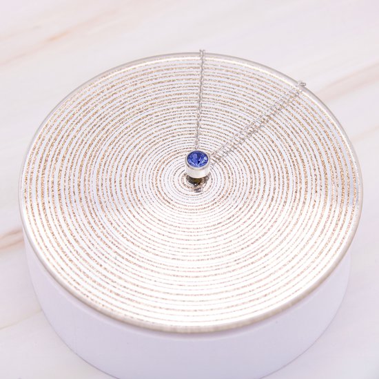 Zilverkleurige ketting met blauwe hanger op een zilveren display.