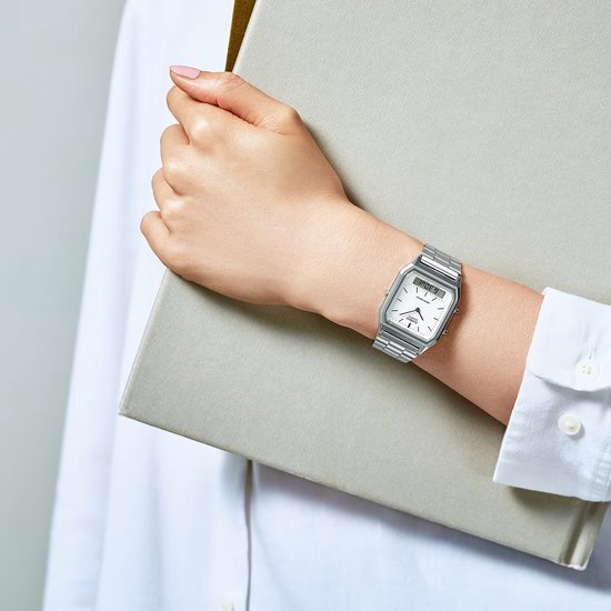 Montre Casio argentée portée au poignet, à côté d'un livre.