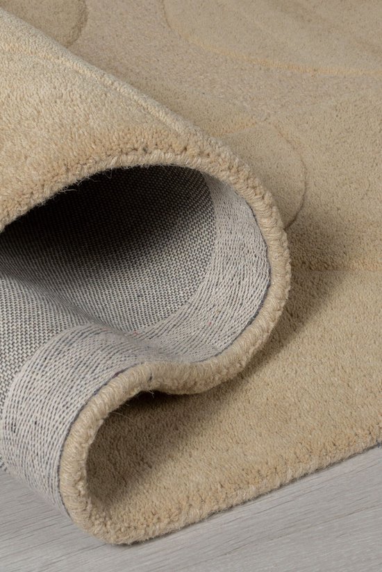 Omgerolde hoek van een zacht beige vloerkleed met een contrasterende grijze onderkant.