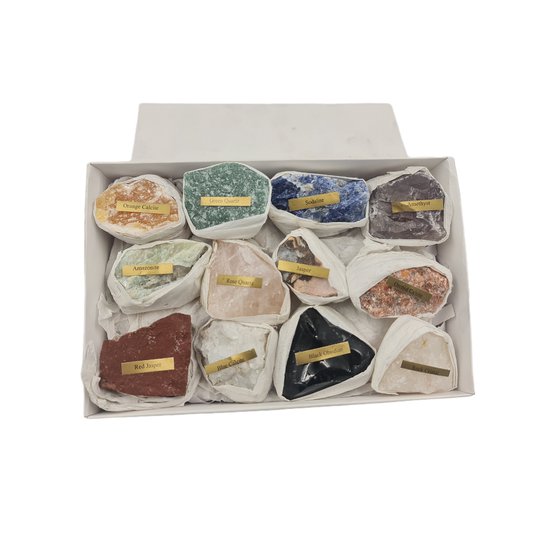 Une boîte blanche ouverte contenant 12 pierres brutes, y compris du calcite orange, du quartz vert, de la sodalite, de l'améthyste, du calcite bleu, du quartz rose et du jaspe rouge.