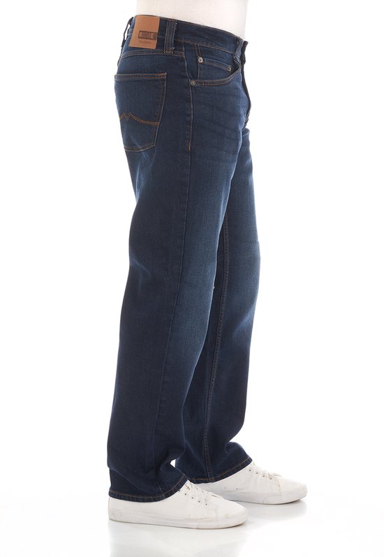 Man in donkerblauwe regular fit jeans met oranje stiksels en witte sneakers.