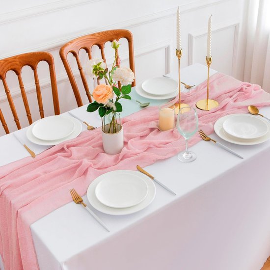 Chemin de table en mousseline rose sur une table dressée avec des fleurs, des bougies et des couverts dorés.