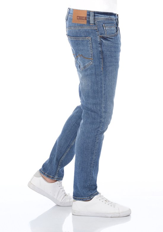 Zijaanzicht van een man in een blauwe jeans met tapered fit. De jeans is licht verkleurd en heeft een bruin leren Mustang label.