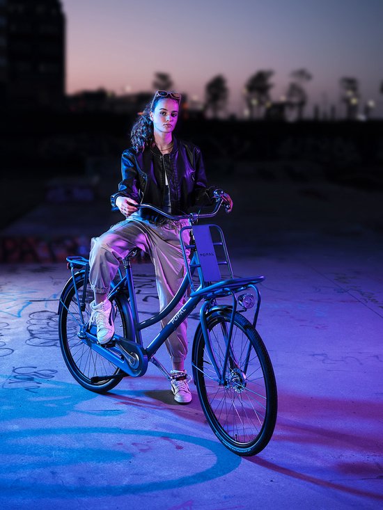 Jonge vrouw met Popal transportfiets in donkerblauw, met voorrek en achterdrager, bij nacht.