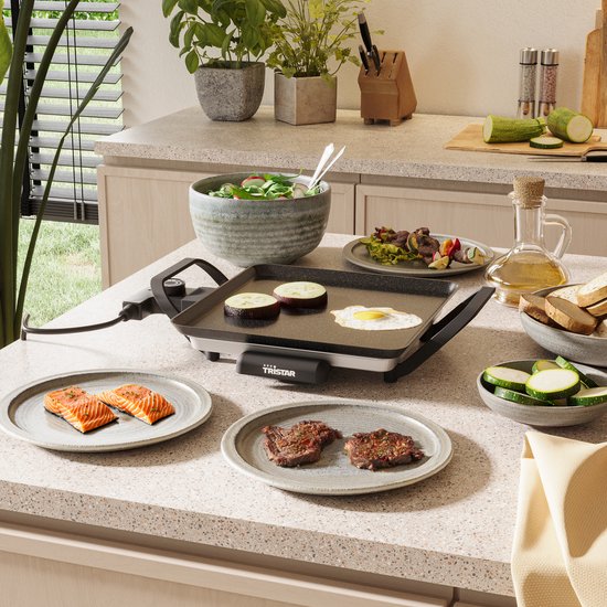 Elektrische grillplaat met zalm en steak, op een aanrecht met ingrediënten.