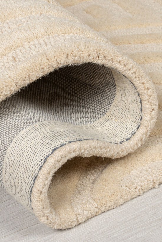 Opgerold beige vloerkleed met een zicht op de achterkant en de beige bovenkant.