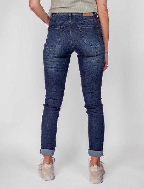Donkerblauwe jeans met lichte wassing, opgerolde broekspijpen, gedragen door een model met beige sneakers.