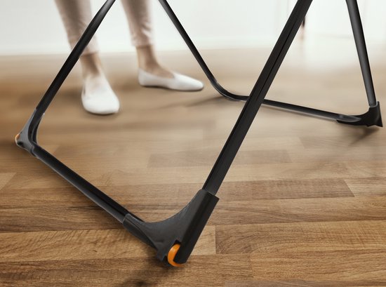 Pieds en chaussures blanches sur un plancher en bois, près des pieds à roulettes d'un séchoir noir.
