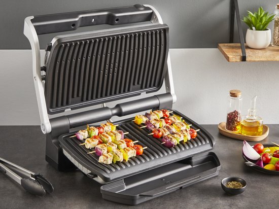 Open contactgrill met spiesjes van kip, paprika en ui op de grillplaten. Ingrediënten en een kruidenmolen staan ernaast.