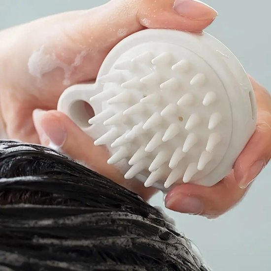 Witte hoofdhuidmassager met nopjes wordt gebruikt om donker haar te masseren, met schuim.