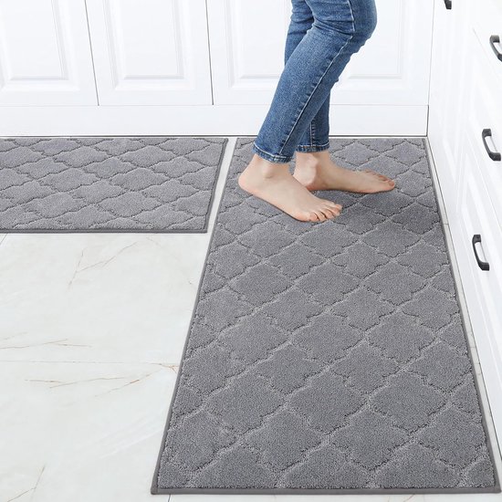 Pieds d'une personne sur un tapis de cuisine gris à motif losange, à côté d'un autre tapis de cuisine gris.