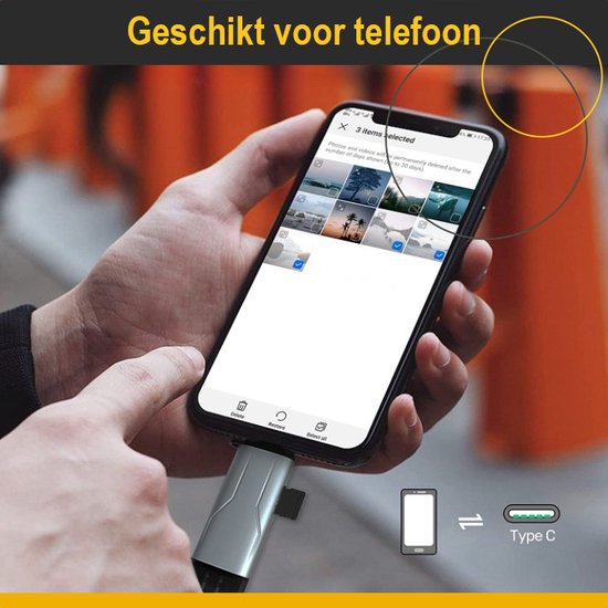 Een hand houdt een telefoon vast met een foto-app open. Een zilveren USB-stick is aangesloten op de telefoon.