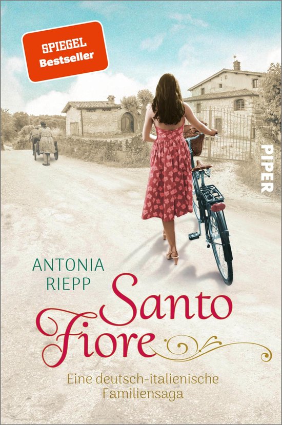 SPIEGEL Bestseller: Een jonge vrouw in een roze jurk met bloemenmotief duwt een fiets over een stoffige weg in een Italiaans dorp. "Santo Fiore" door Antonia Riepp.