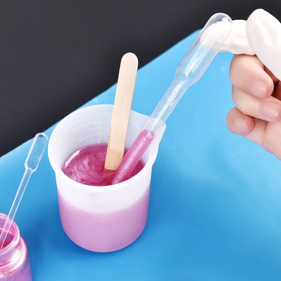 Une main tenant une pipette aspire un liquide rose scintillant dans un petit bécher.