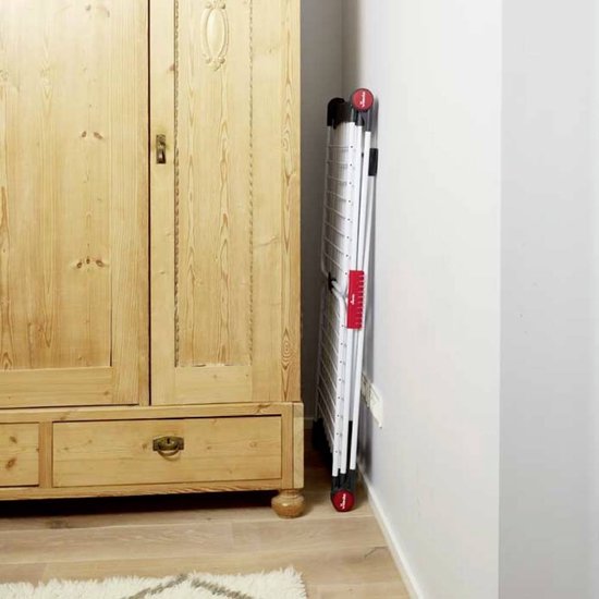Étendage Vileda Infinity Flex plié, debout contre un mur à côté d'une armoire en bois.