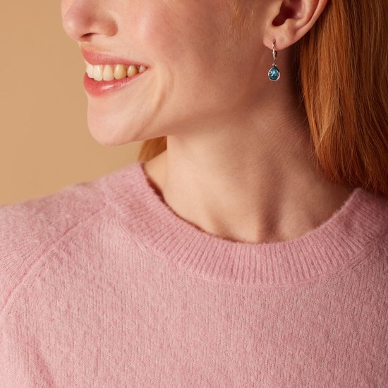 Boucles d'oreilles goutte d'eau bleues en cristal sur une bélière argentée, portées par un mannequin avec un pull rose.