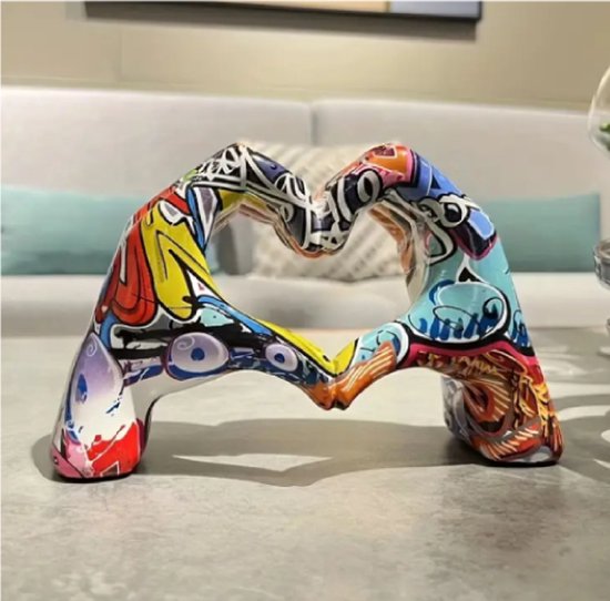 Deux mains forment un cœur, peintes de graffitis colorés, sur une table.