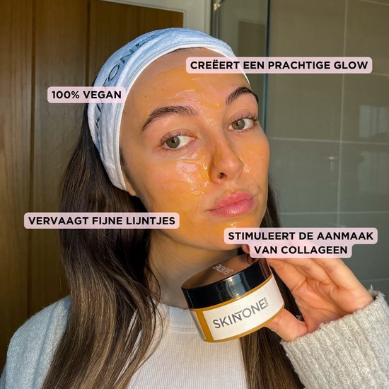 Vrouw met een oranje gelmasker op haar gezicht en een potje "SKINTONE" in haar hand.