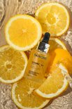 SKINONE vitamine C serum flesje omringd door partjes en schijfjes van sinaasappel en citroen in water.