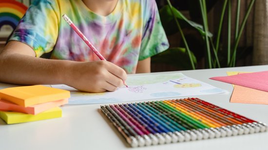 Kind kleurt met een roze potlood, naast een regenboog van potloden.