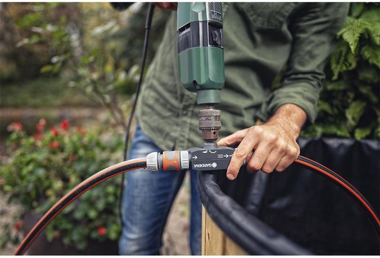 Close-up van man die met boormachine GARDENA voorzetpomp bevestigt aan tuinslang.