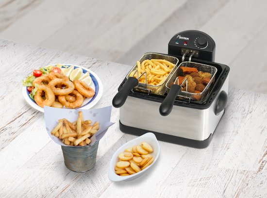 RVS frituurpan met twee mandjes, op een houten tafel. Naast de frituurpan staan friet, bitterballen, calamaris en gebakken aardappeltjes.