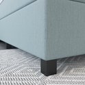 Onderkant lichtblauwe boxspring op een geometrisch tapijt met donkere poten.