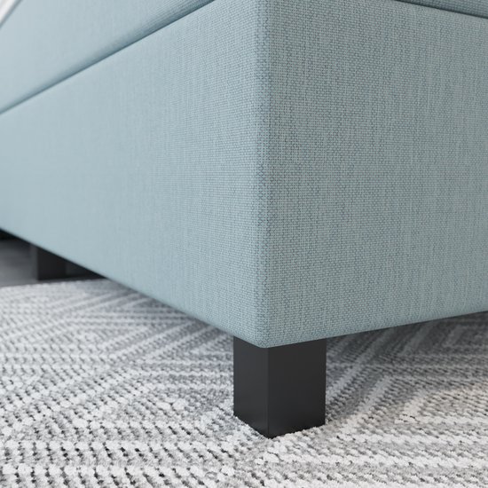 Onderkant lichtblauwe boxspring op een geometrisch tapijt met donkere poten.