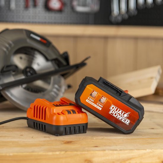 Oranje Dual Power accu op oranje lader, naast een cirkelzaag.