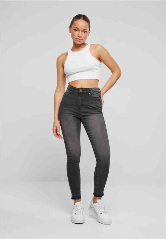 Model draagt een zwarte wassing skinny high waist jeans met rafelige zoom en witte top.