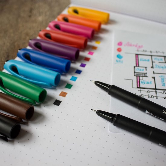 Verschillende gekleurde doppen van fineliners liggen naast een schets van een plattegrond. Twee zwarte fineliners liggen op het papier.