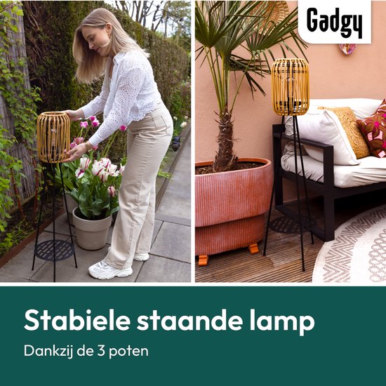 Vrouw plaatst rotan lantaarn in de tuin. De lamp staat stabiel op 3 poten.