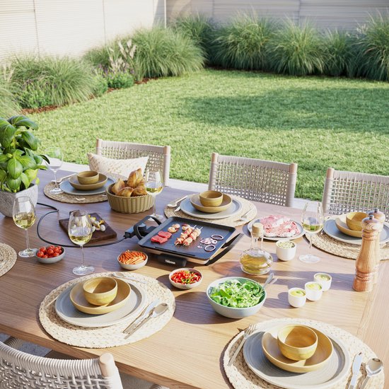Gourmetstel op een tuintafel met eten en stoelen, buiten.