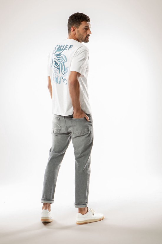 Man met op de rug een witte T-shirt met blauw blad-print "CHIEF". Grijze jeans.