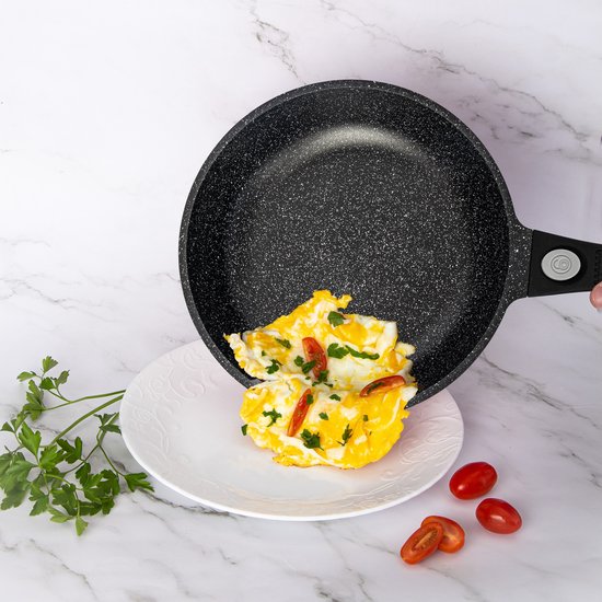 Een zwarte Royalty Line koekenpan met marmeren anti-aanbaklaag wordt gebruikt om een omelet met groenten te bakken.