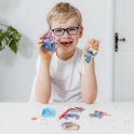 Un garçon avec des lunettes tient deux magnets Stitch diamond painting terminés : un avec deux Stitch violets et un avec Stitch aux accents jaunes.